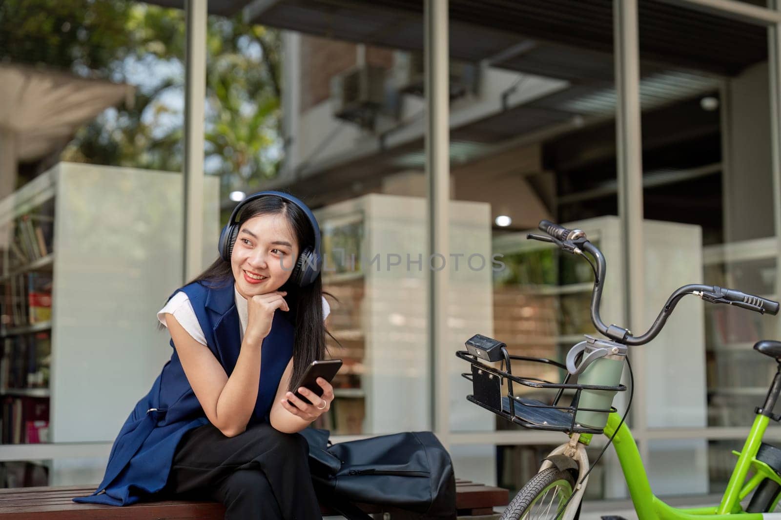Smiling businesswoman with headphones relaxing with her bicycle outside office. Concept of modern urban commuting, relaxation, and productivity.