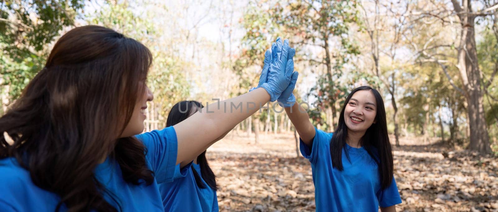 Female volunteer high fiving in forest. Concept of teamwork, unity, and environmental service.