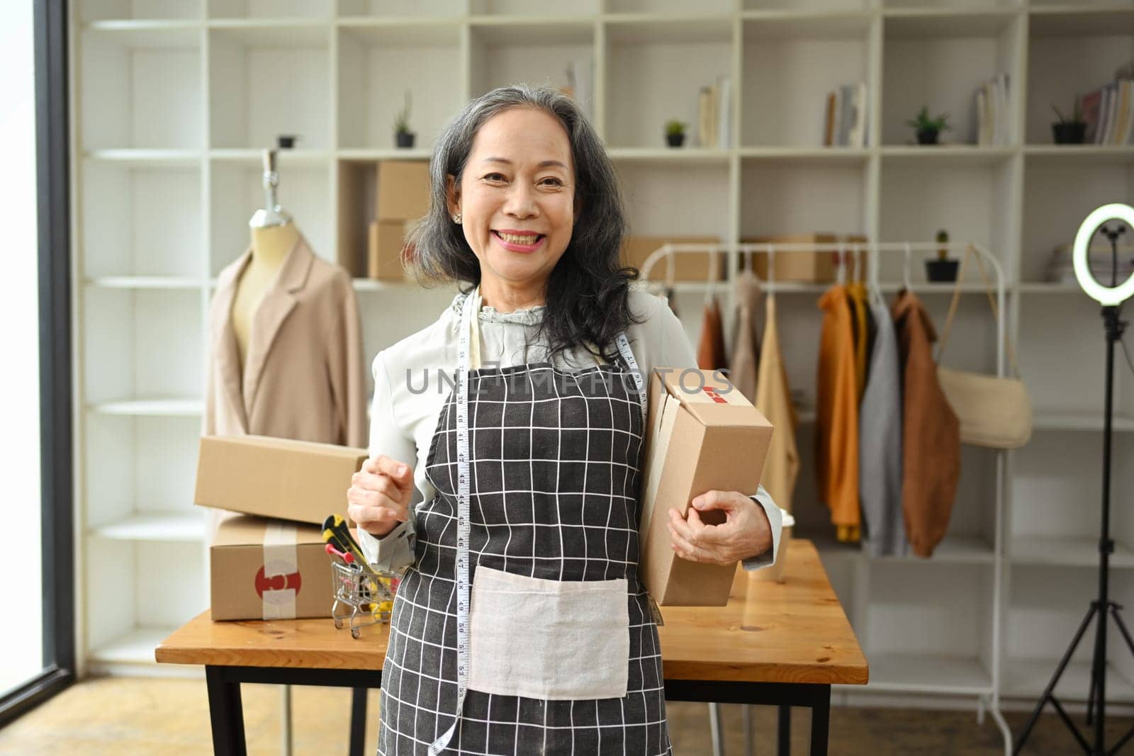 Successful small business owner smiling cheerfully holding cardboard box standing in her shop.