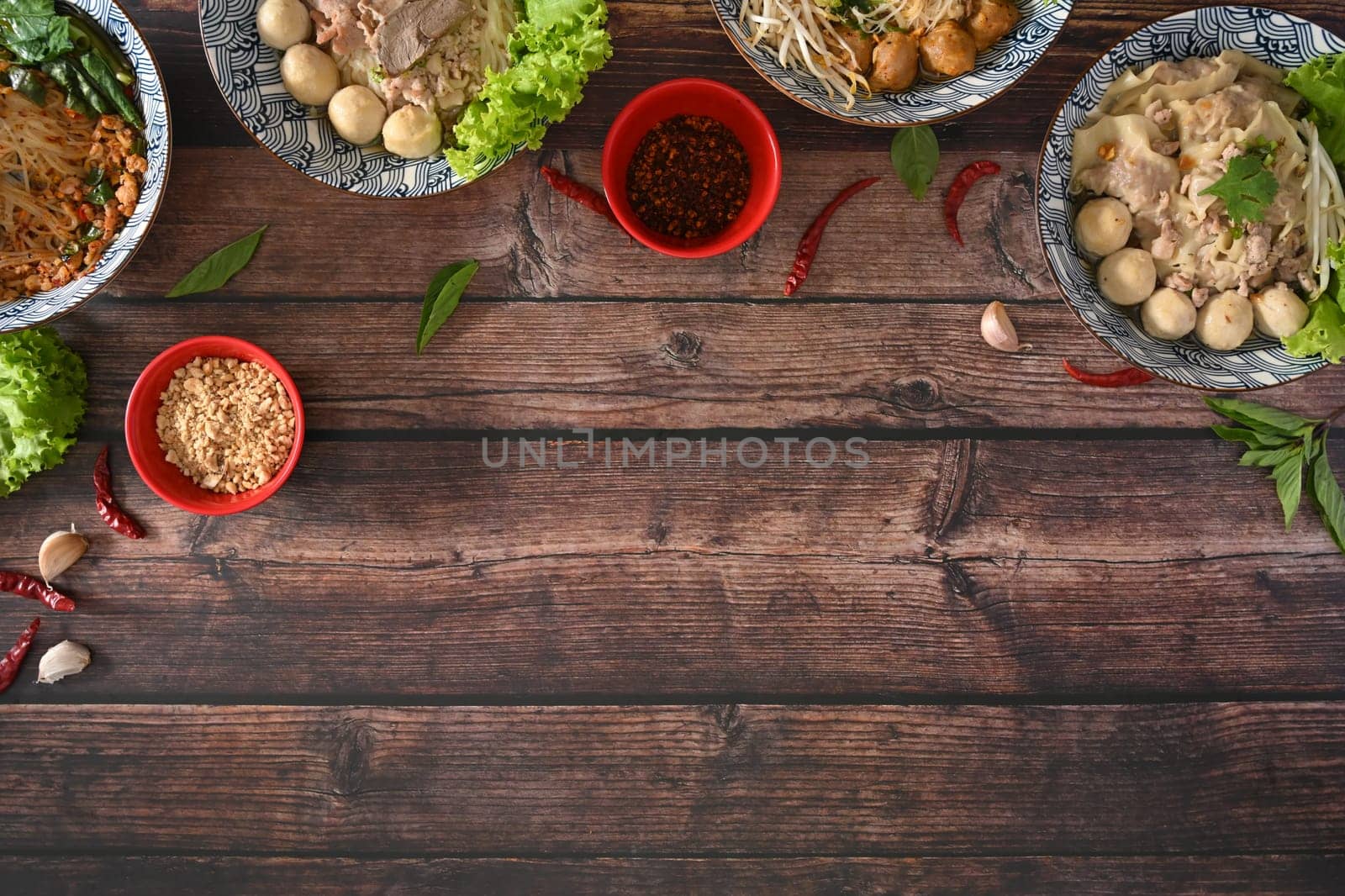 Spicy Thai noodles, dumpling soup on wooden table with ground peanuts and chili powder. Top view with copy space.