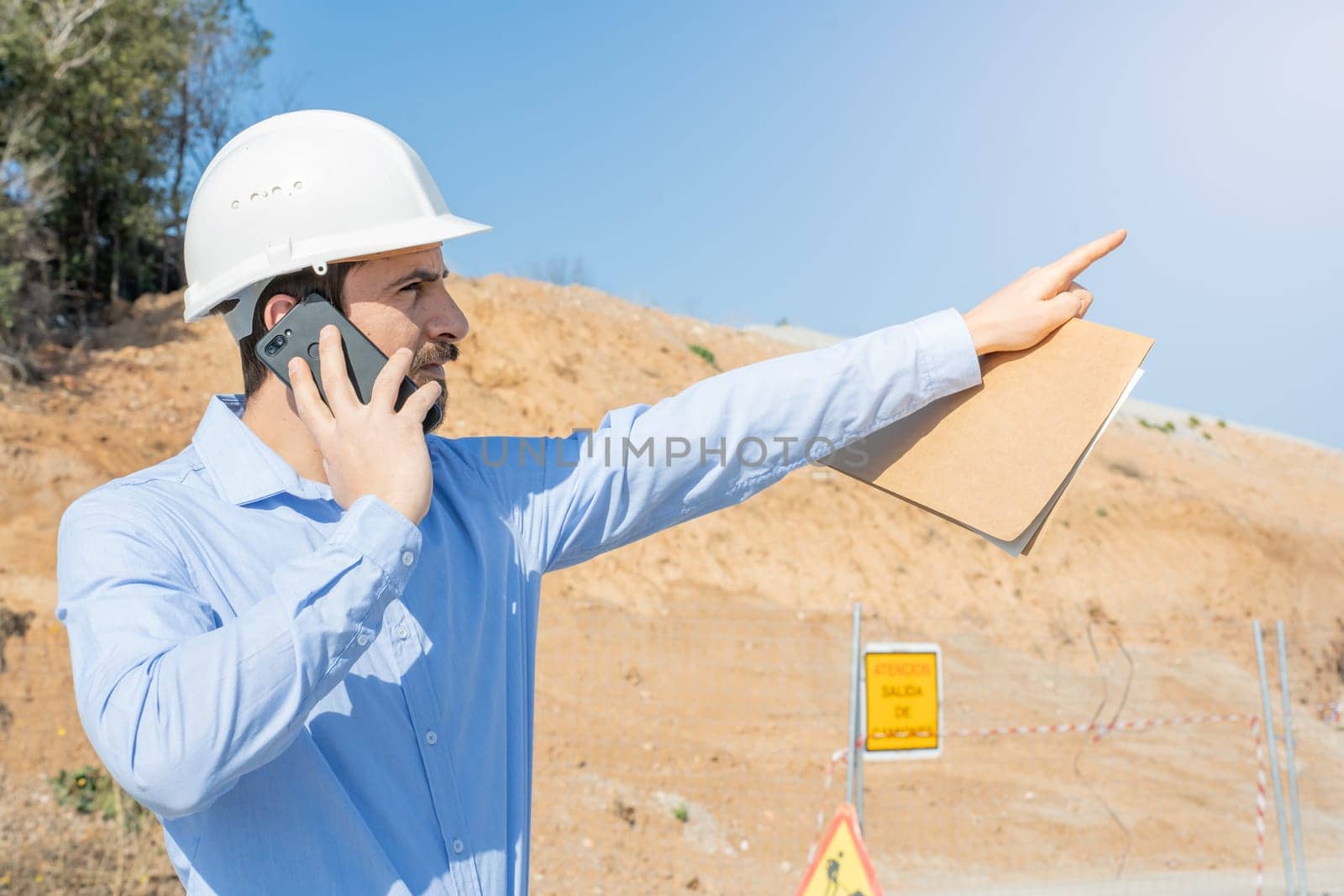 architect working on a construction with plans and using mobile phone. High quality photo