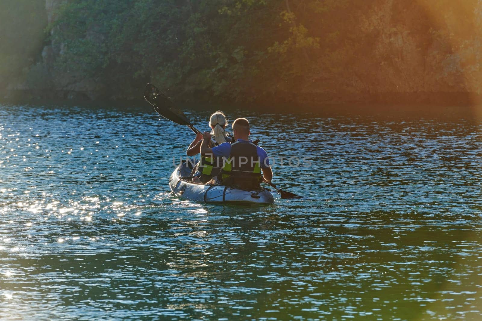 A young couple enjoying an idyllic kayak ride in the middle of a beautiful river surrounded by forest greenery in sunset time by dotshock