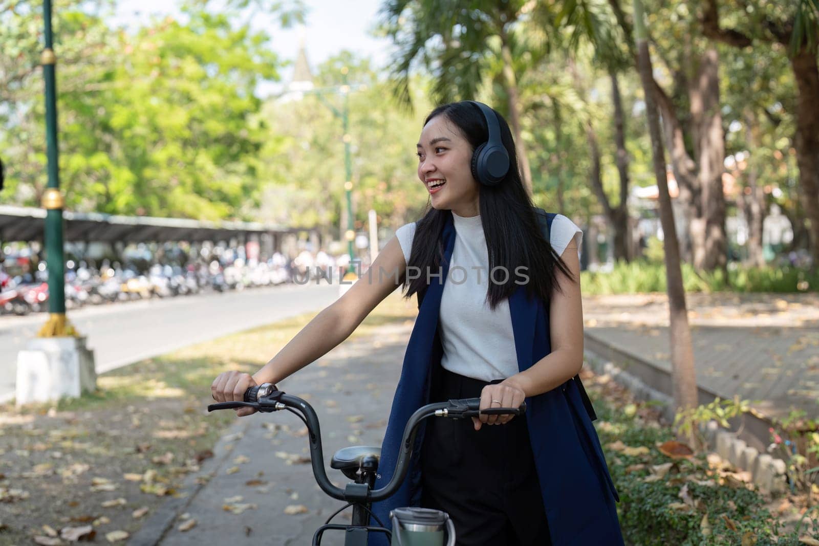 Businesswoman commuting by bicycle with headphones in urban park. Concept of eco friendly transport, active lifestyle, and outdoor fitness.