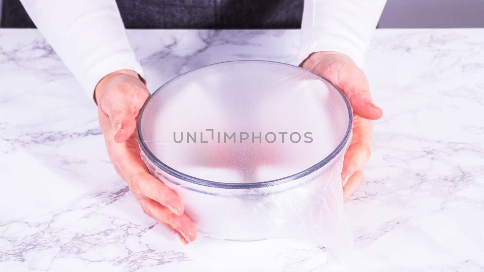 Strawberries, freshly washed and dried, are neatly stored in a glass bowl lined with a paper towel and securely covered with plastic wrap to maintain freshness.