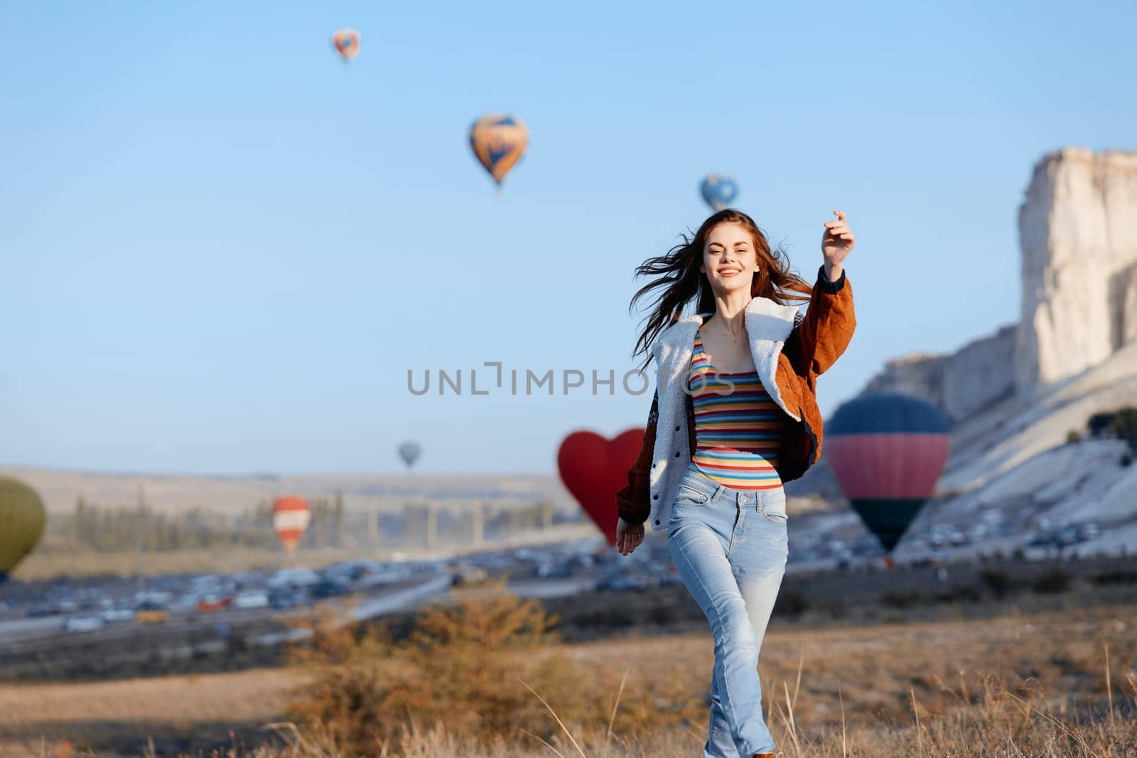 Carefree young woman captures moment in field with balloons and mountain backdrop
