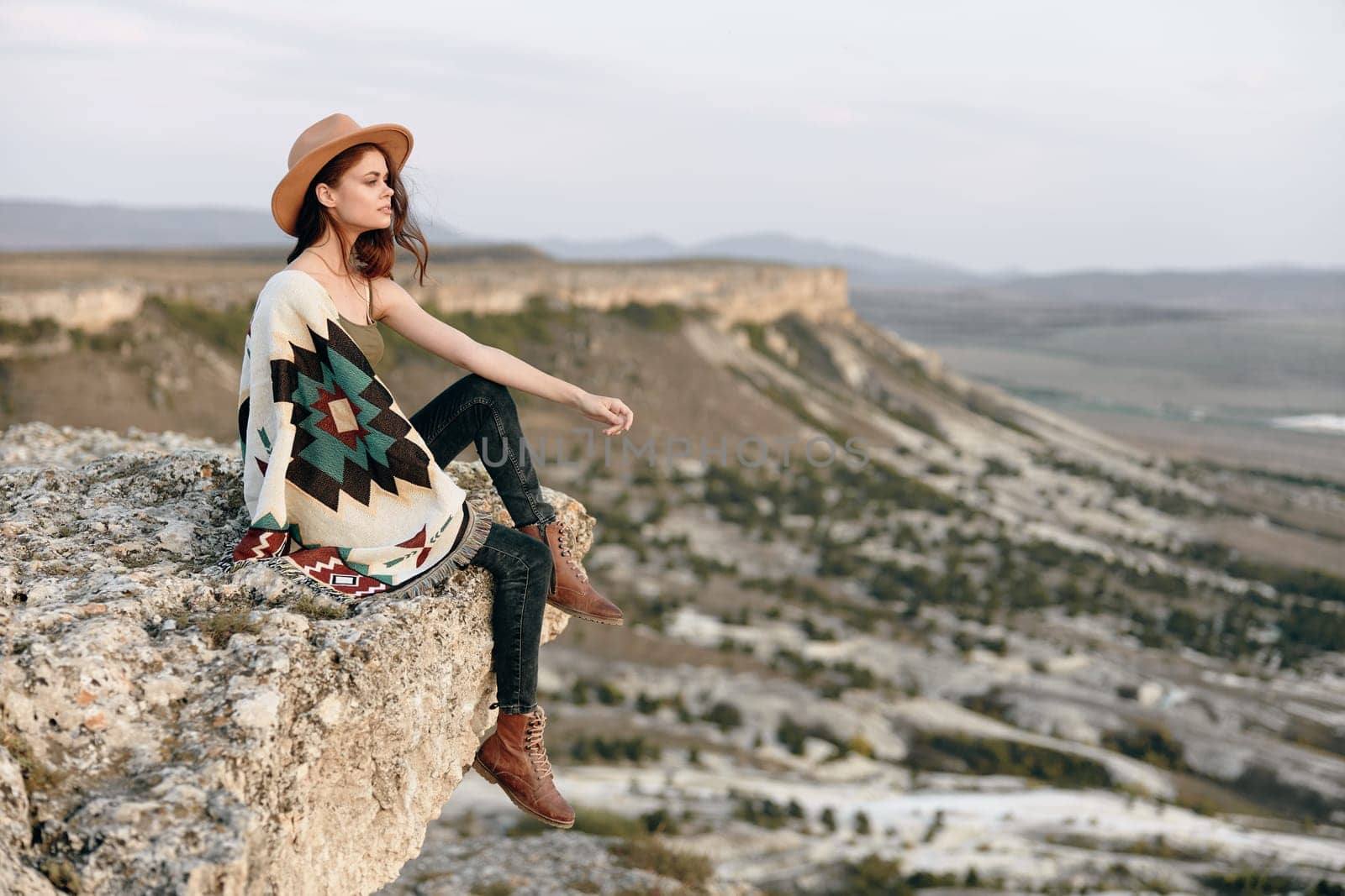 serene woman enjoying the view from mountain peak wrapped in a cozy blanket and wearing a hat