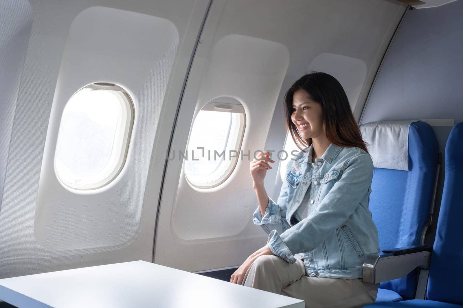 Asian woman smiling while sitting by airplane window. Concept of air travel, relaxation, and leisure by wichayada