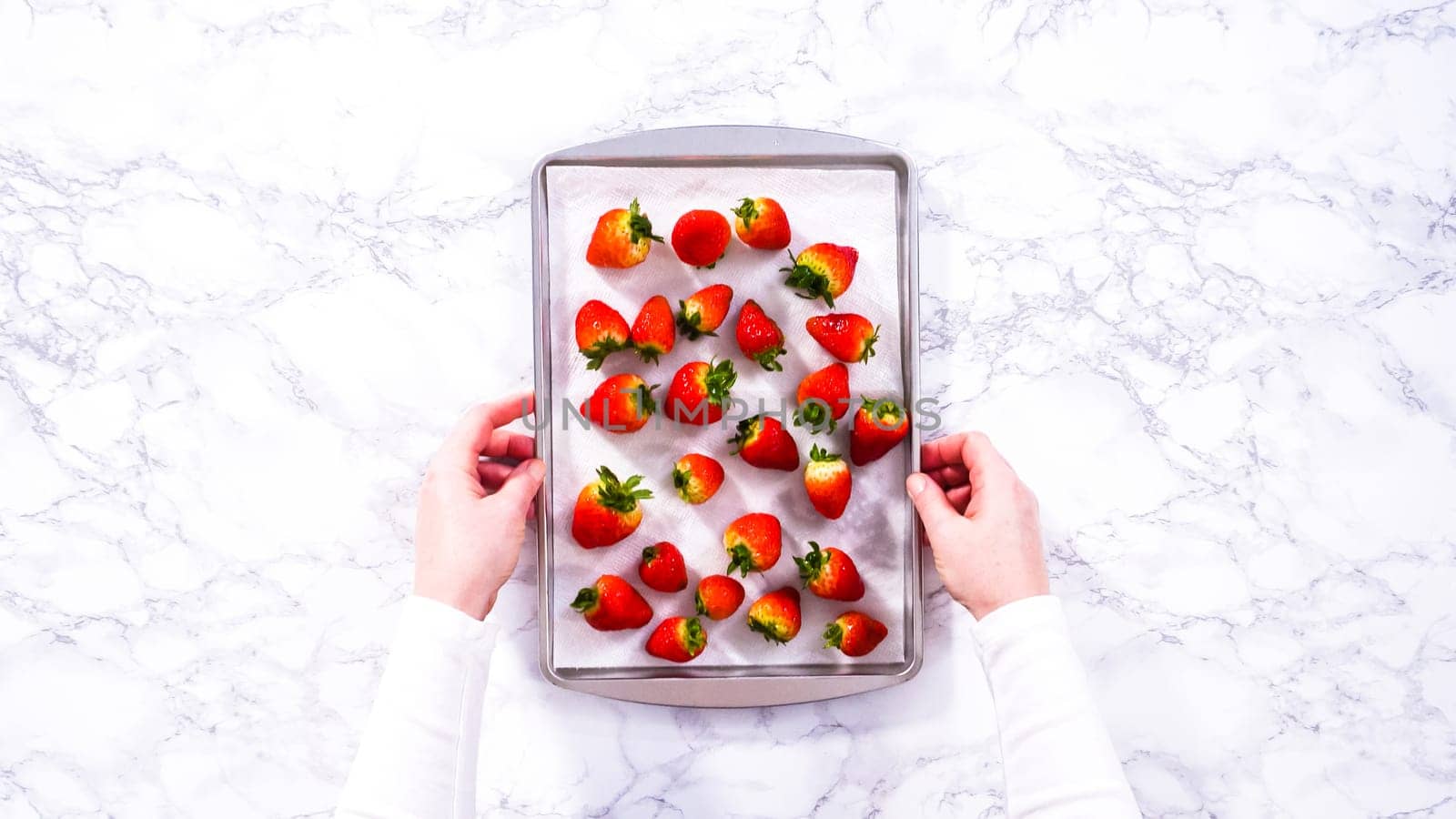 Flat lay. Juicy red strawberries, freshly washed, are spread out to dry on a baking sheet, carefully lined with paper towels to absorb excess moisture and prevent mold.