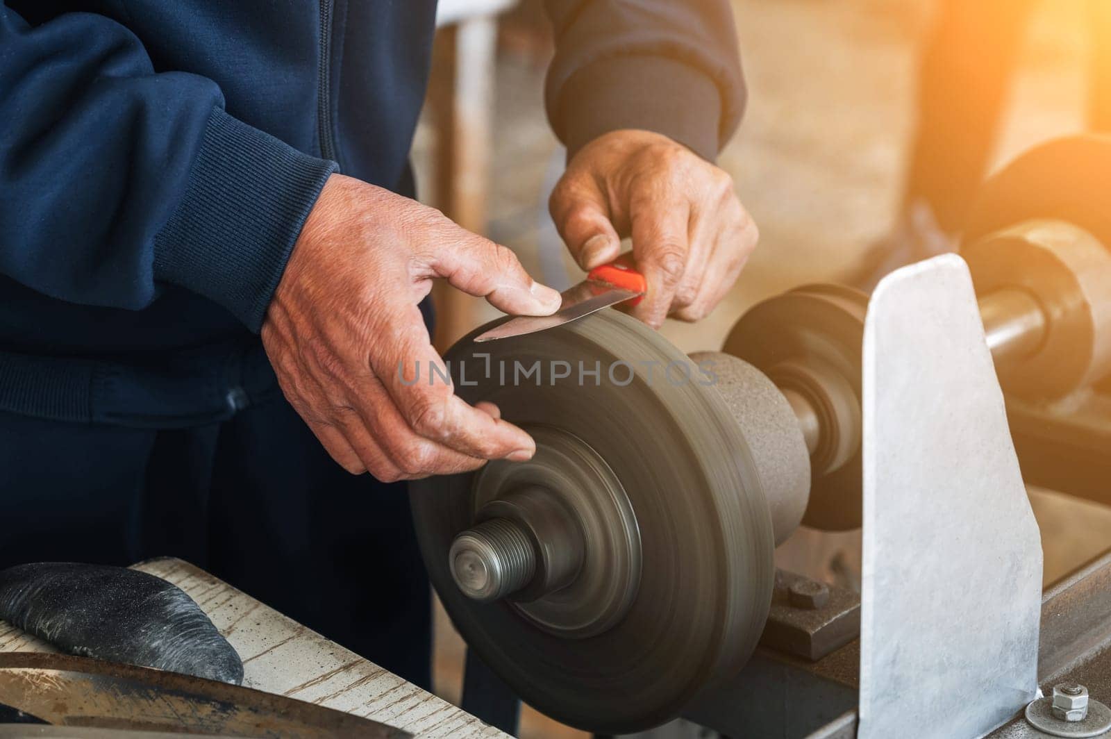 male sharpener grinder sharpens a knife blade on a sharpening machine with rotating abrasive wheel close-up