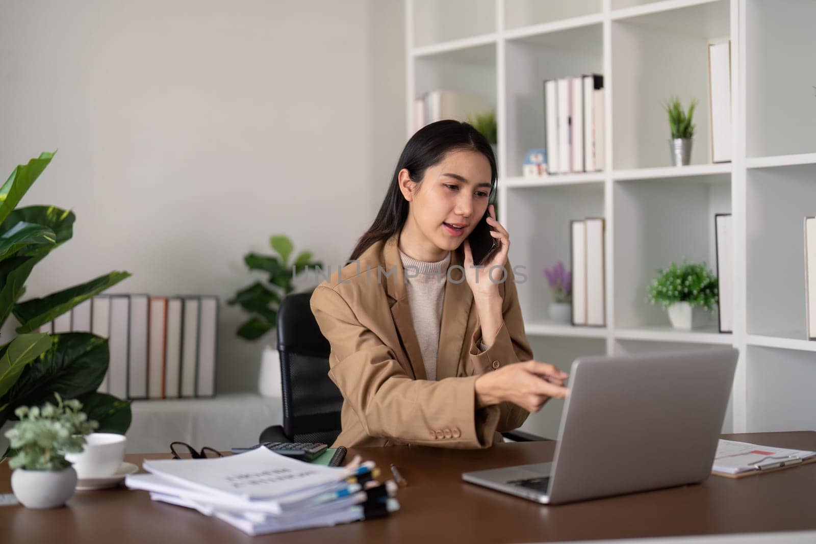 Businesswoman discussing work on phone at desk with laptop. Concept of professional communication and office productivity.