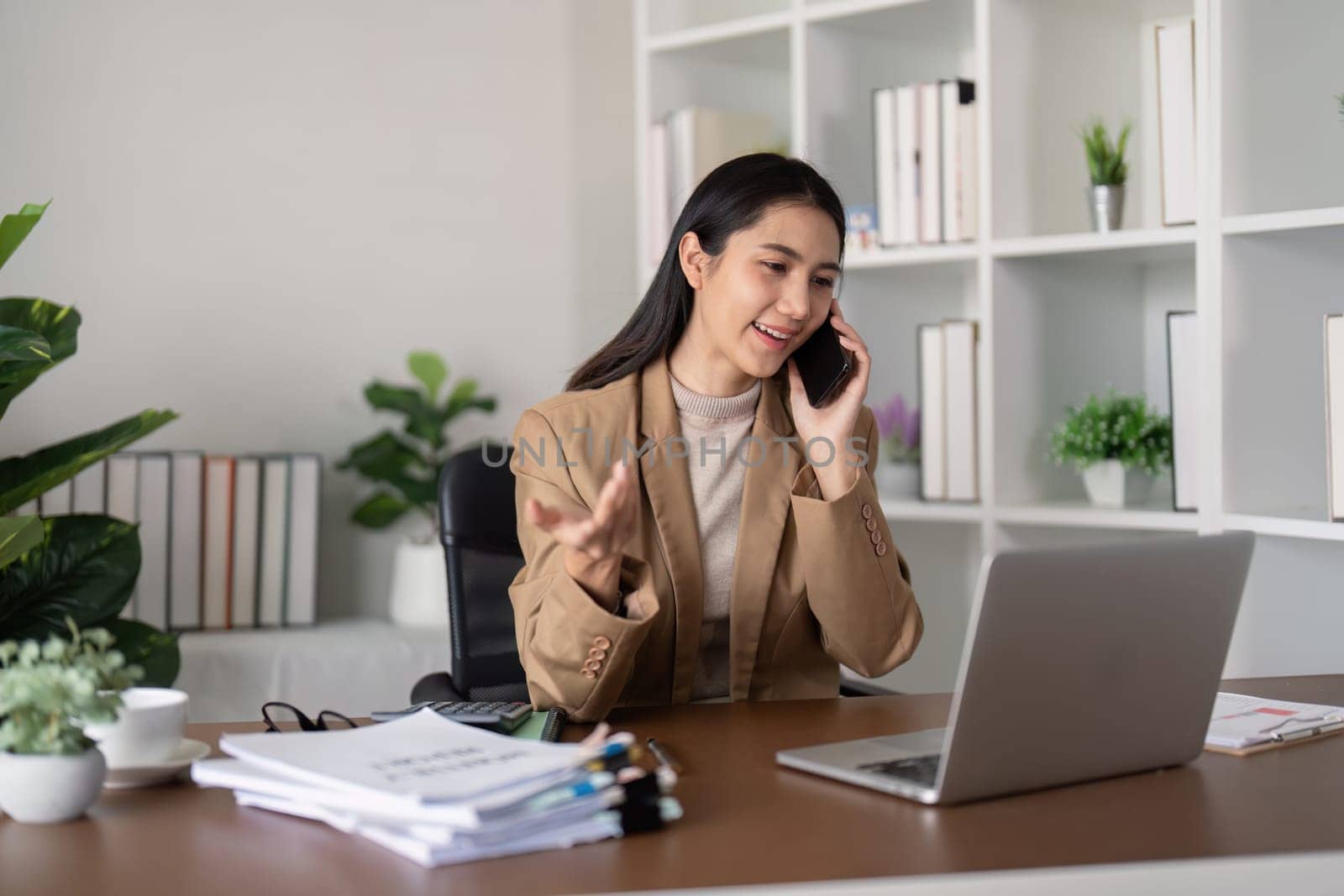 Smiling businesswoman on phone call at desk with laptop. Concept of professional communication and office work.