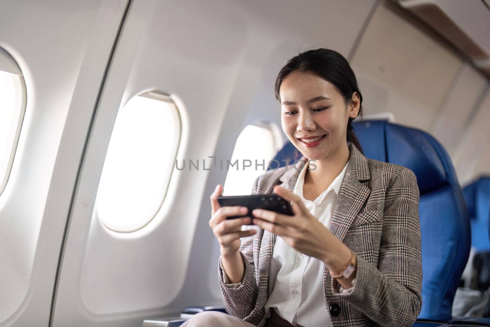 Smiling businesswoman using smartphone on airplane. Concept of in flight communication and business travel.