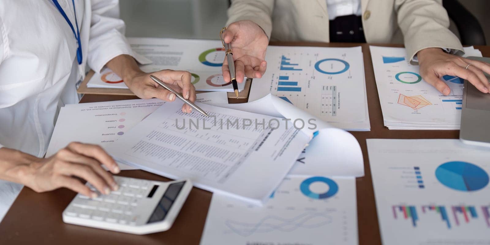 Hands of businesswomen working on financial reports with calculator and charts. Concept of data analysis, teamwork, and financial planning.