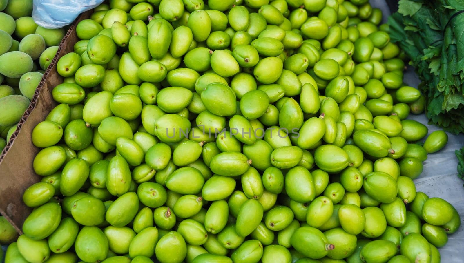 unripe green apricot on counter of a bazaar in Uzbekistan. Traditional Uzbek food on the market shelf - green uryuk, dovcha, gura