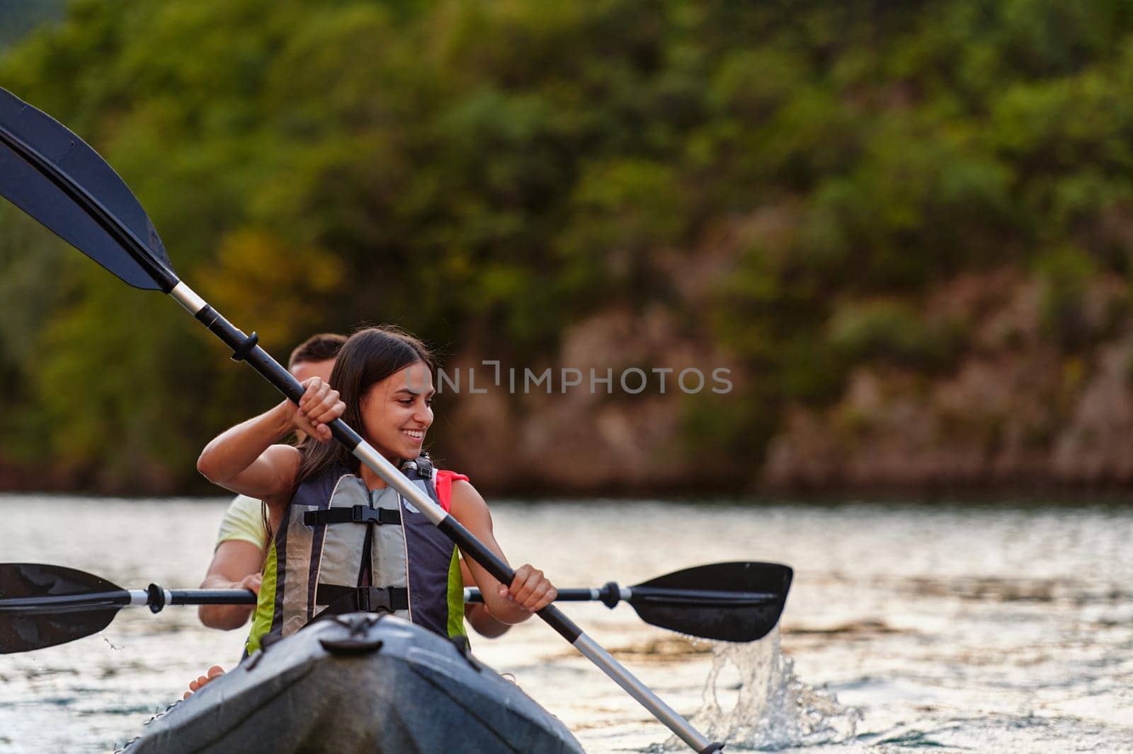 A young couple enjoying an idyllic kayak ride in the middle of a beautiful river surrounded by forest greenery.