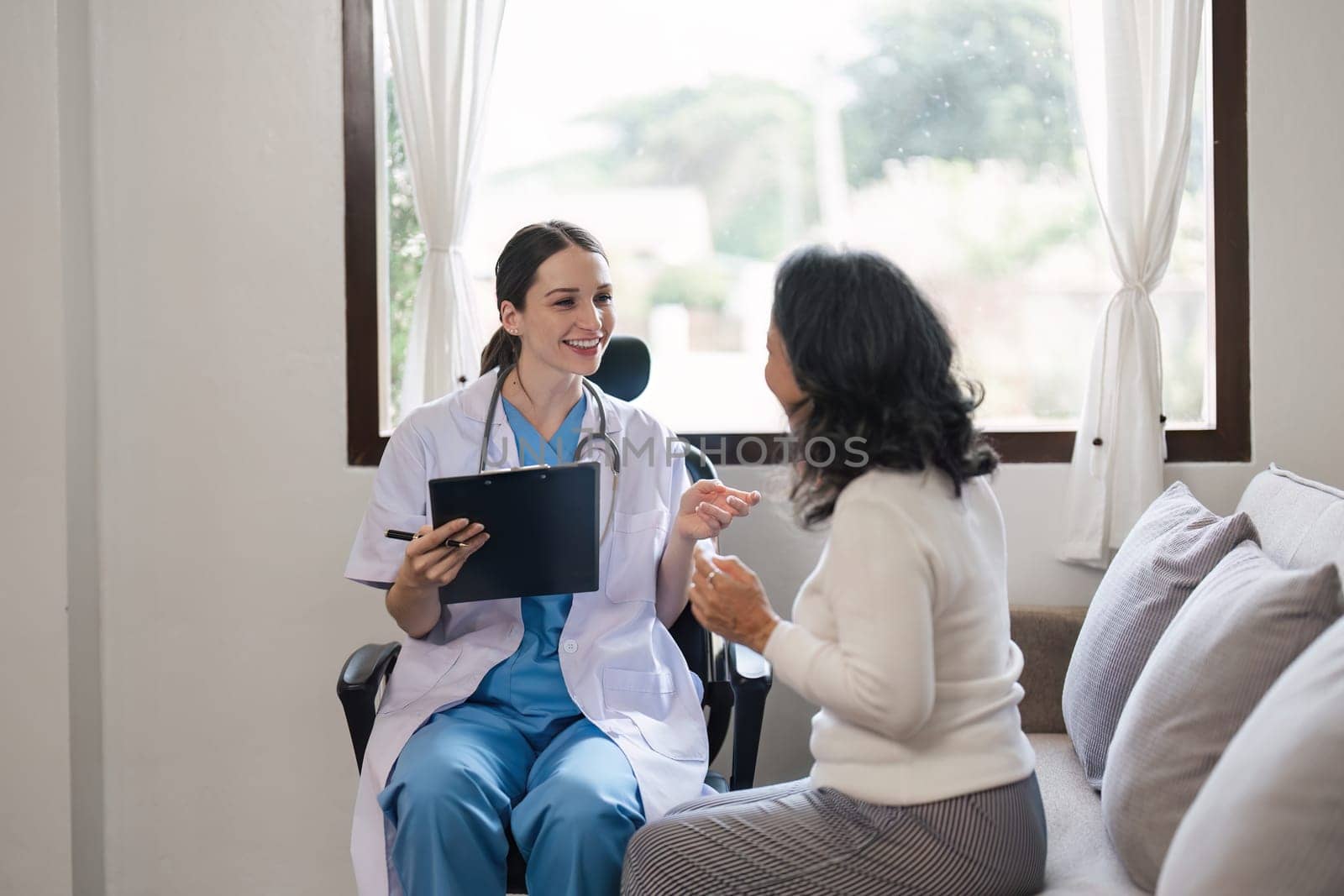 Doctor consulting with senior woman on sofa in home. Healthcare and patient support concept.