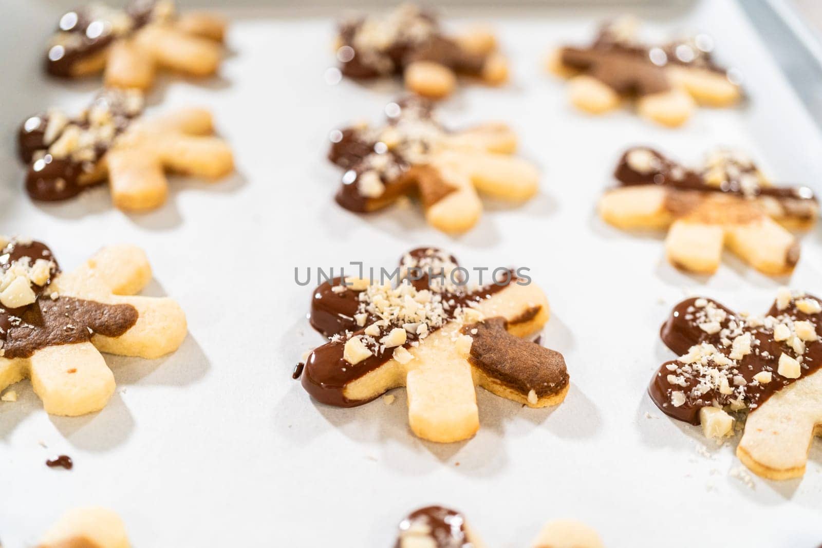 Creating cutout sugar cookies, partially dipped in chocolate and topped with hazelnut pieces, placed on parchment paper.