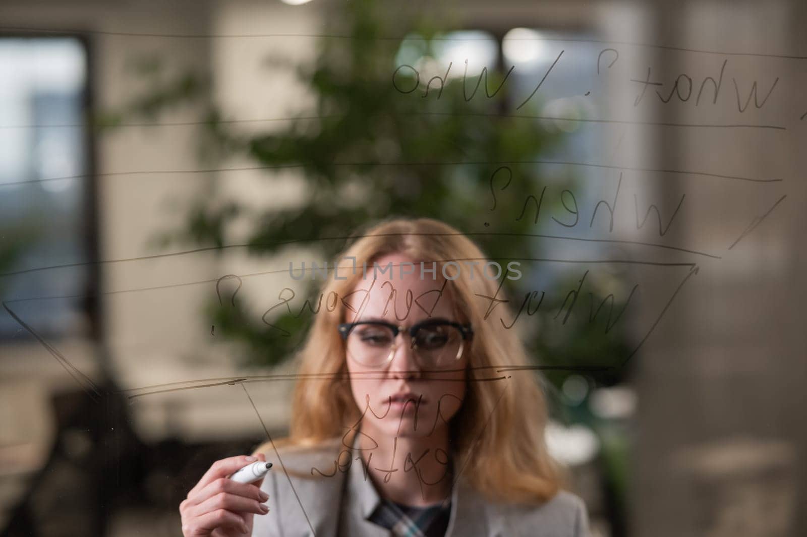 Caucasian woman writing pyramid diagram with questions on glass wall