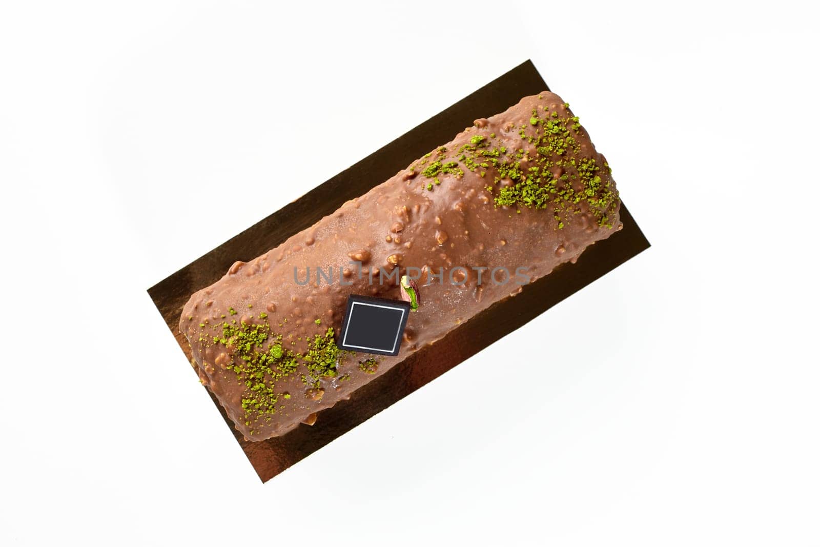 Top view of delicious artisanal loaf cake coated with milk chocolate and nuts glaze, decorated with pistachio crumble and dark chocolate branding plaque, isolated on white. Sweet pastries concept