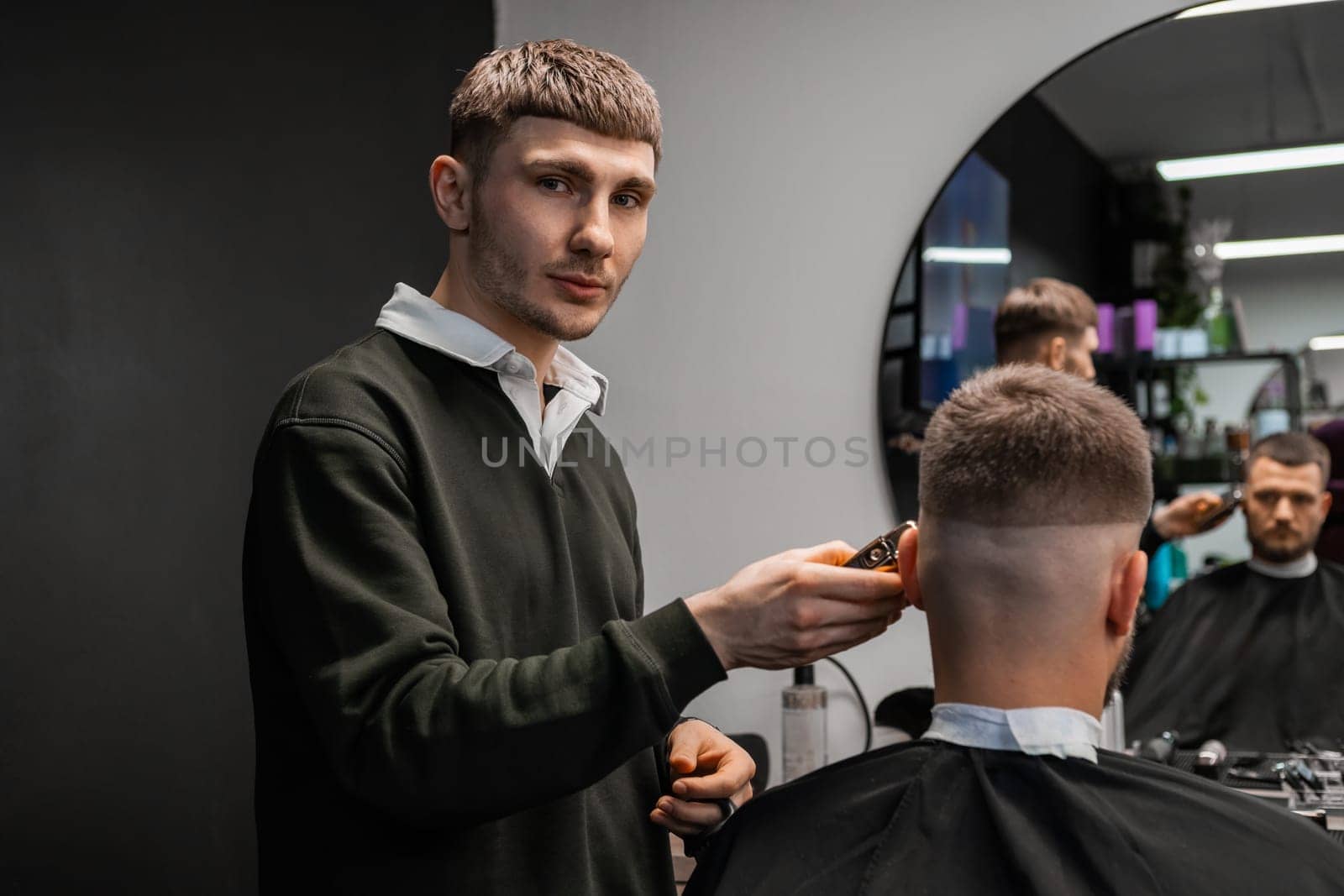 Portrait of young barber diligently styles a mans hair in the barbershop