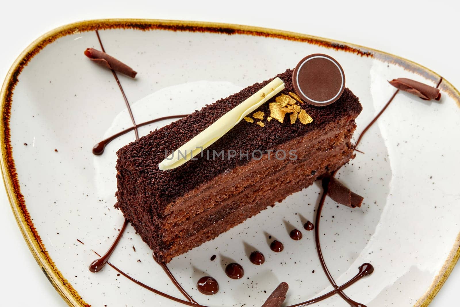 Chocolate truffle cake slice with gold caramel chips on plate by nazarovsergey