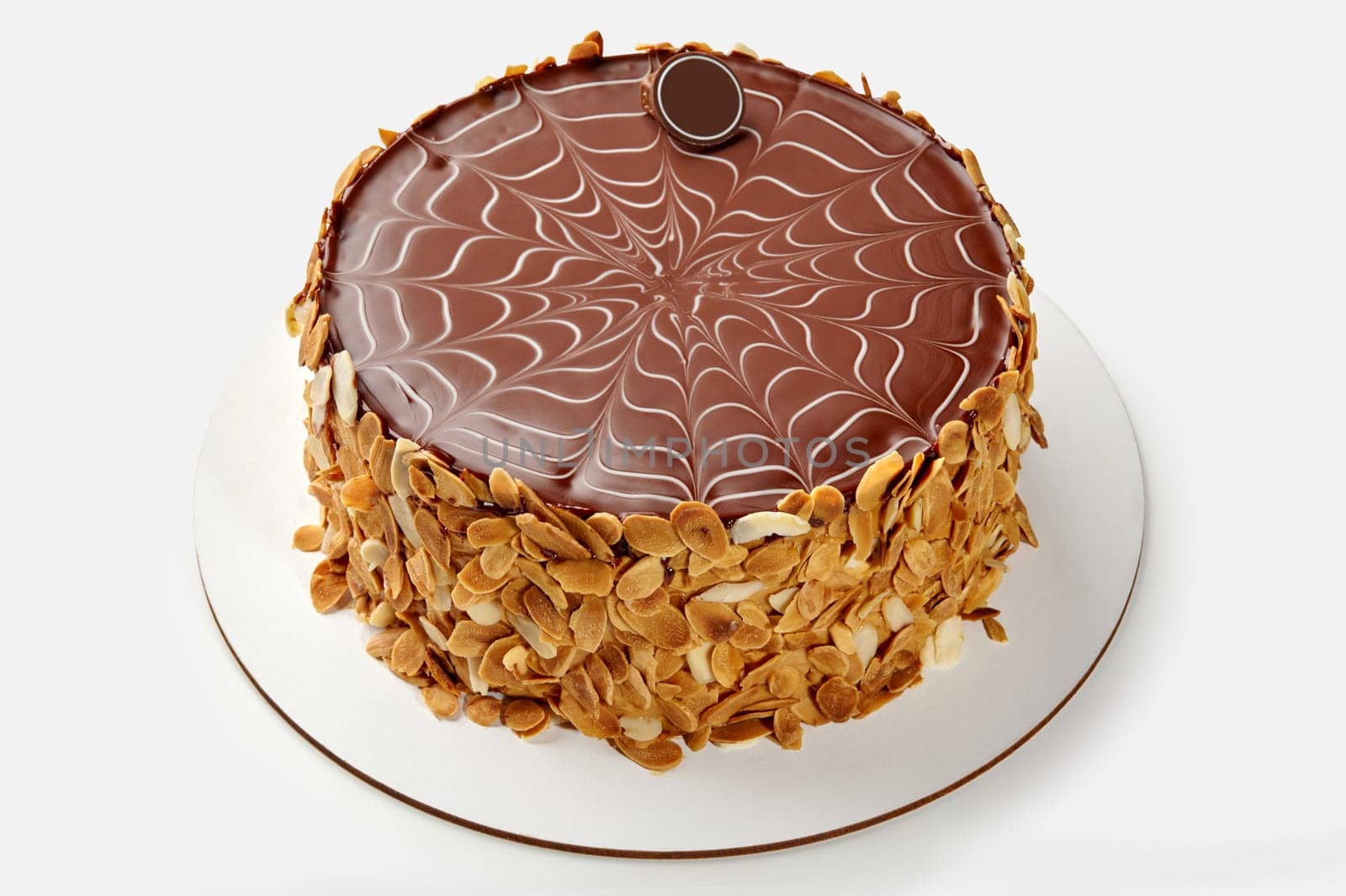 Classic Esterhazy cake with smooth, intricate chocolate icing pattern on top and crunchy almond flake coating around sides, on white backdrop. Confectionery craftsmanship