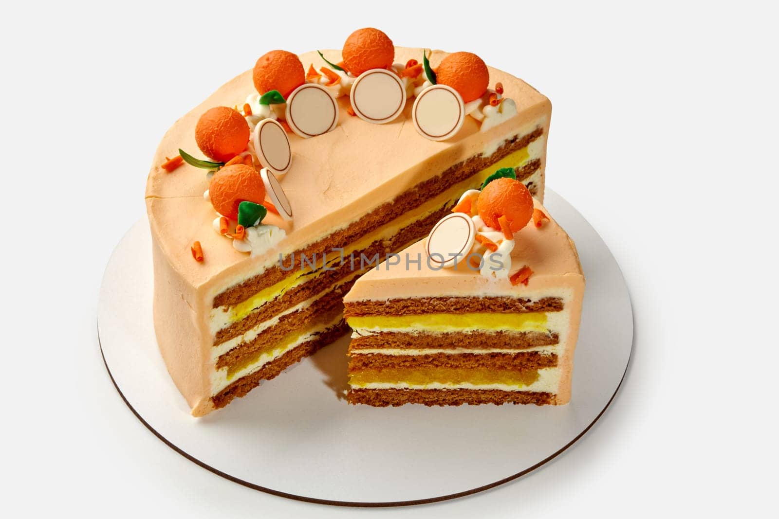 Sliced delicate honey cake with whipped sour cream and citrus confit layers decorated with colorful chocolate oranges with green leaves, presented on white background