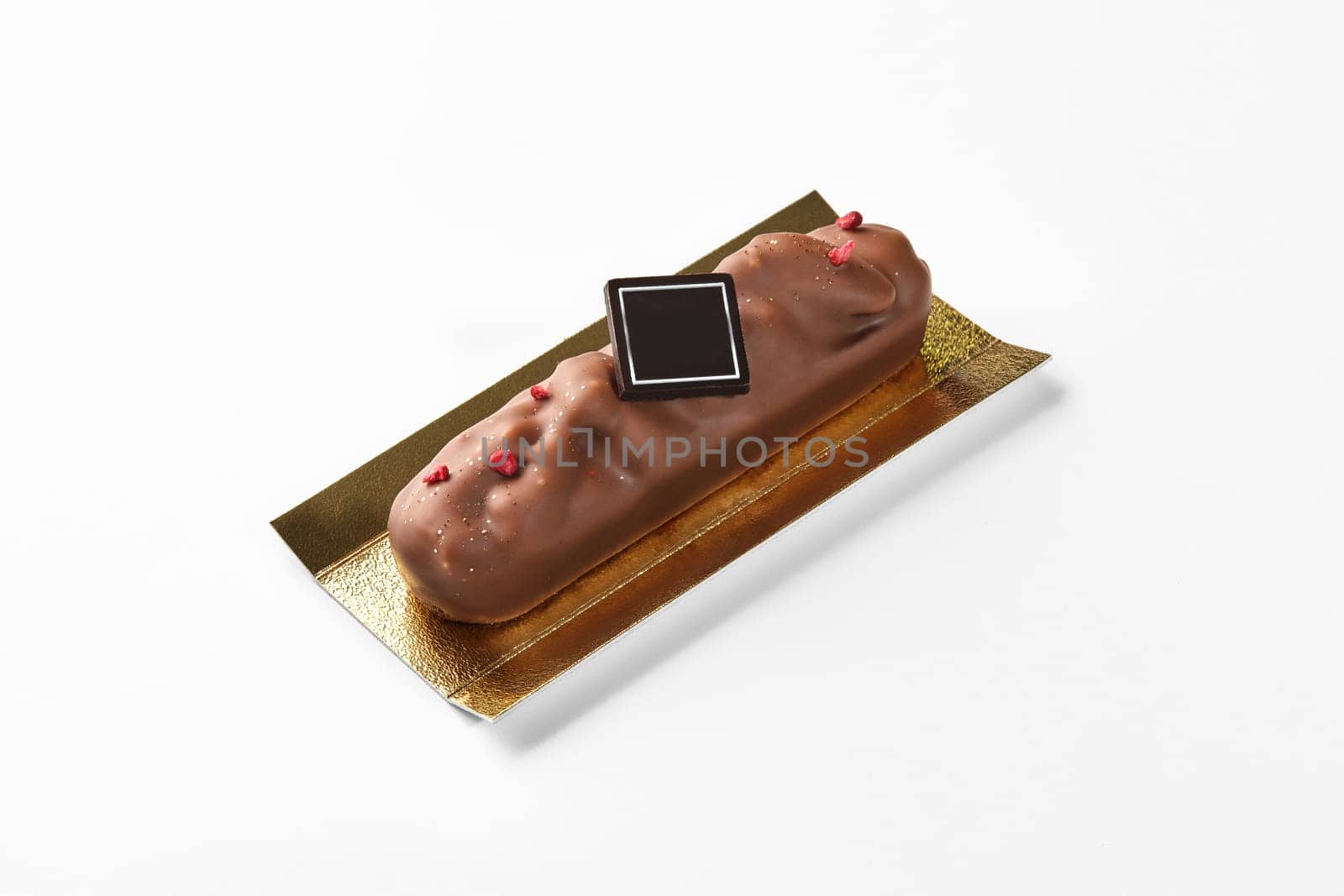 Appetizing milk chocolate bar with pecan decorated with dried berry crumbs and branding dark chocolate plaque on golden cardboard, against white background