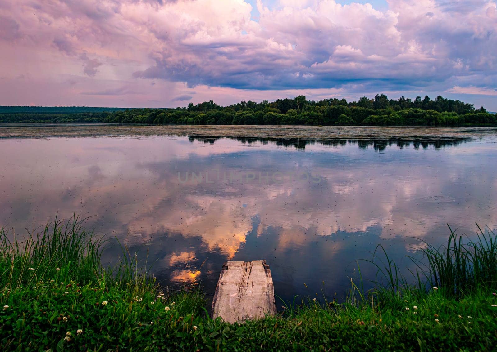 A serene countryside scene during sunset, showcasing a tranquil lake with a wooden dock in the foreground.