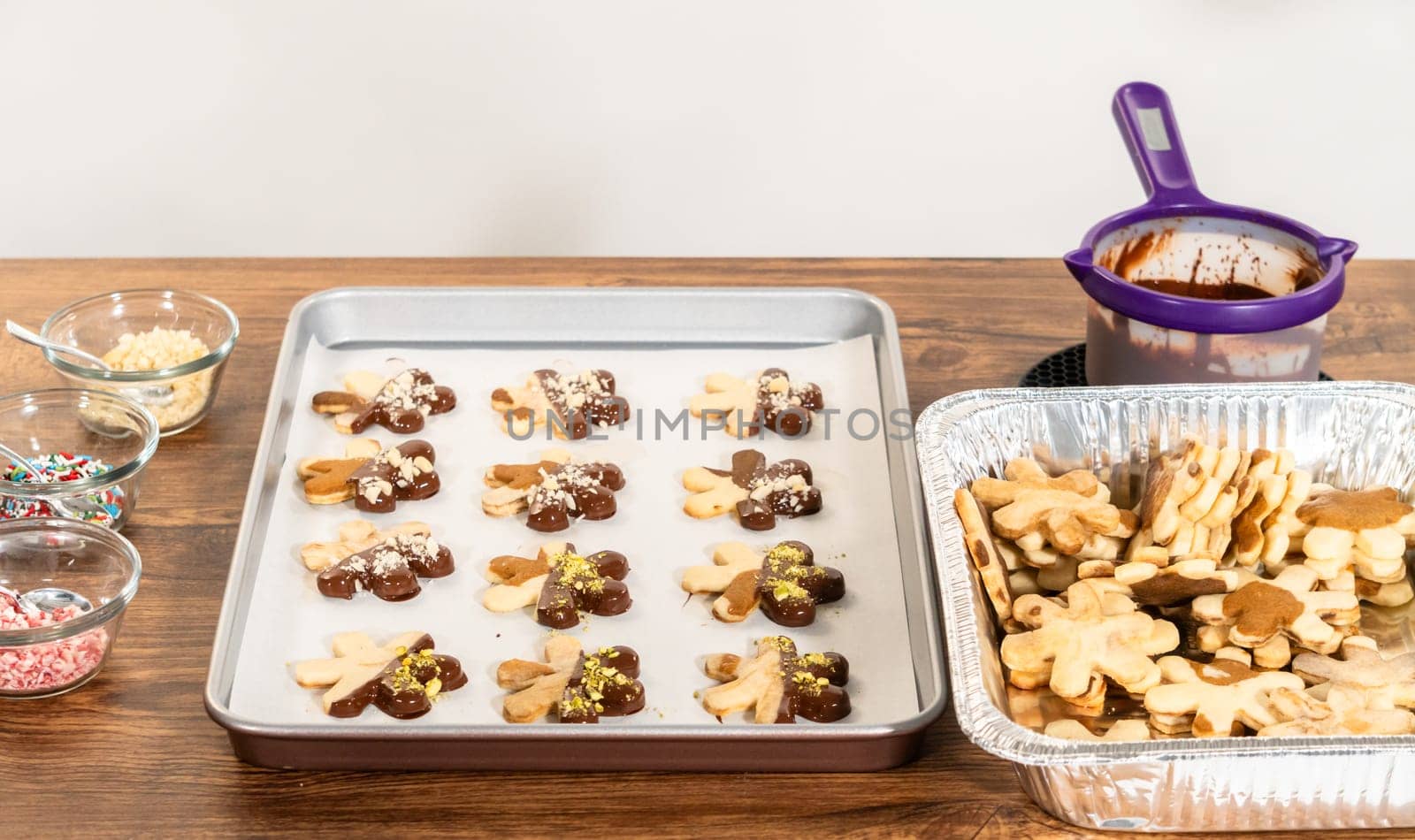 Crafting star-shaped holiday cookies dipped in chocolate and sprinkled with crushed pistachios, arranged on parchment paper.