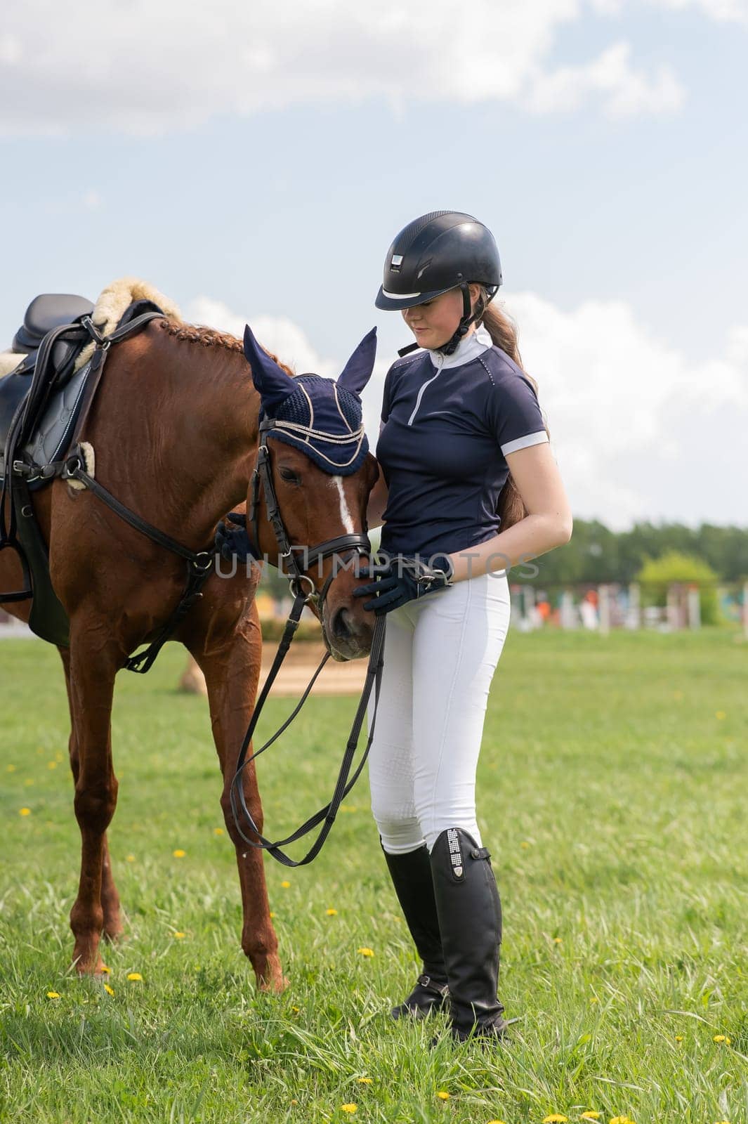 A young girl stands next to a horse before an equestrian competition. Vertical photo