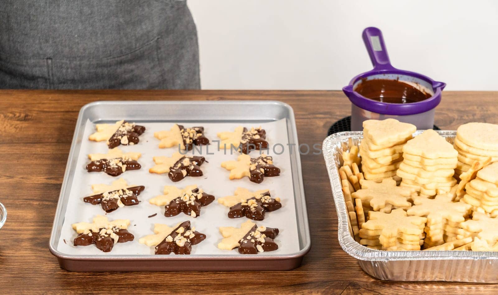 Creating cutout sugar cookies, partially dipped in chocolate and topped with hazelnut pieces, placed on parchment paper.