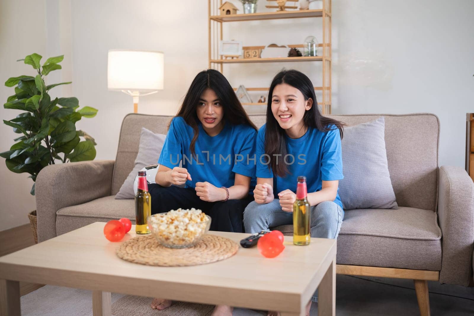 Asian women cheering while watching soccer game at home. Concept of sports, excitement, and friendship. by wichayada