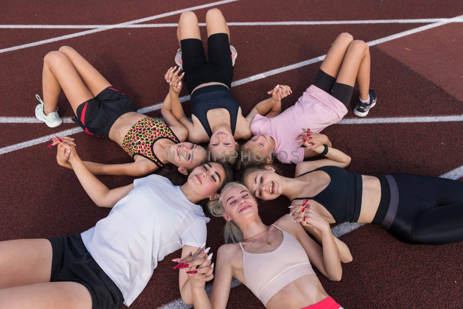 Group of tired and happy fit young girls resting on floor at stadium