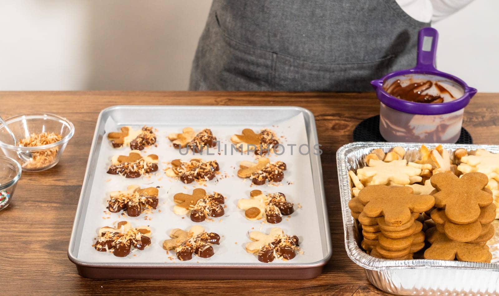 Gingerbread men cookies, chocolate-dipped feet, generously sprinkled with golden toasted coconut shavings, artfully arranged on parchment paper.