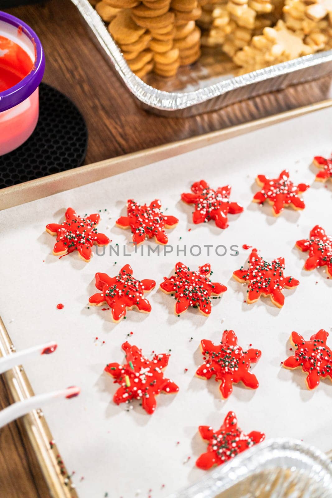 Vivid red star-shaped cookies, generously iced and speckled with green and white holiday sprinkles, freshly prepared and laid out to dry.