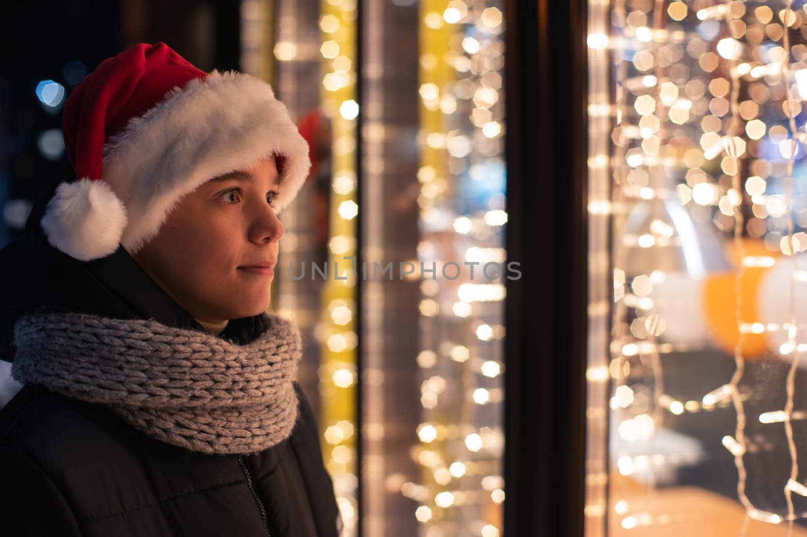 Teen Boy in Santas hat looking and dreaming in illuminated shop window. Xmas presents holidays, or shopping on New Year or Christmas concept