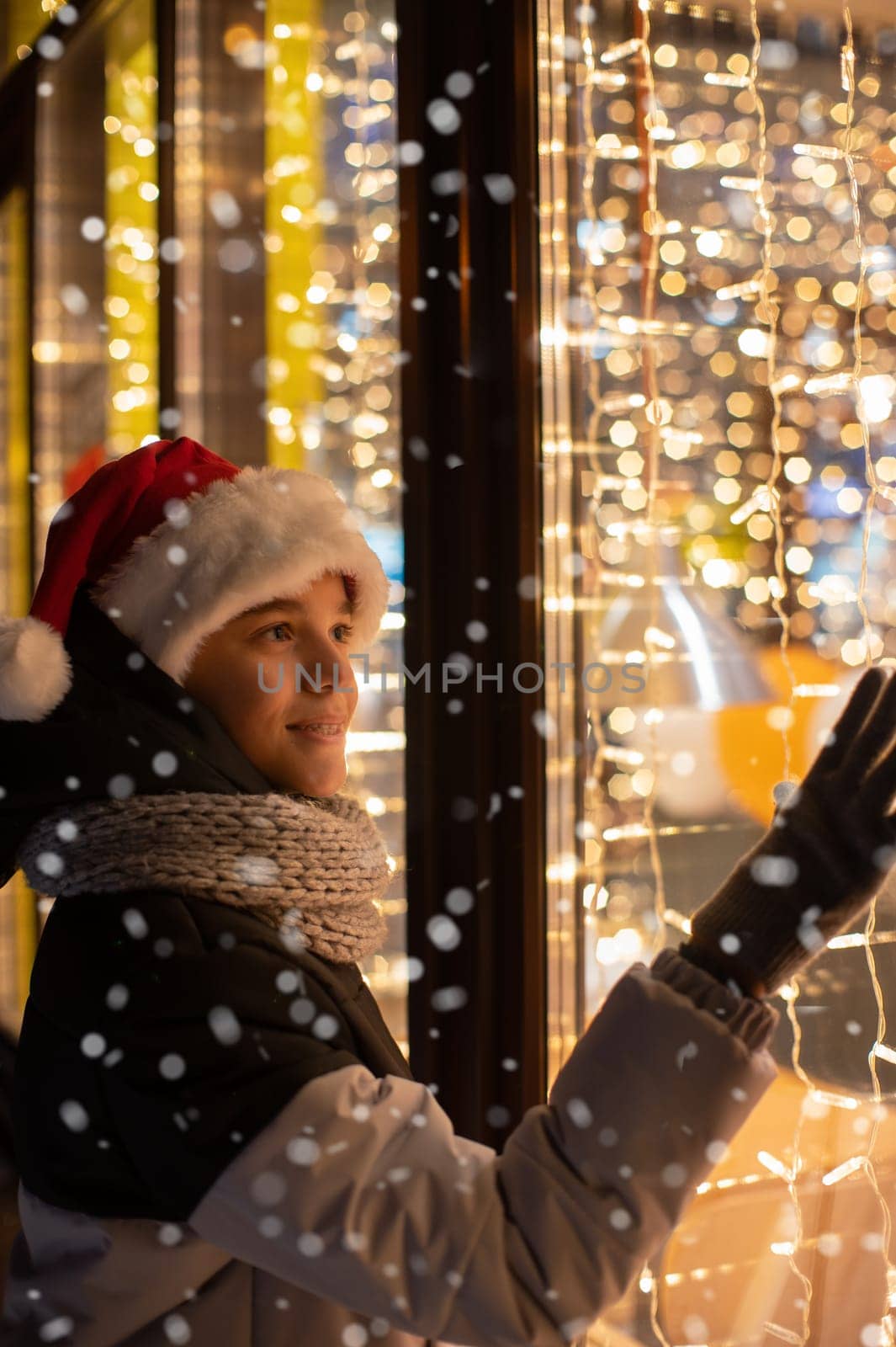 Boy in Santas hat looking and dreaming in illuminated shop window. Xmas presents holidays, or shopping on New Year or Christmas concept