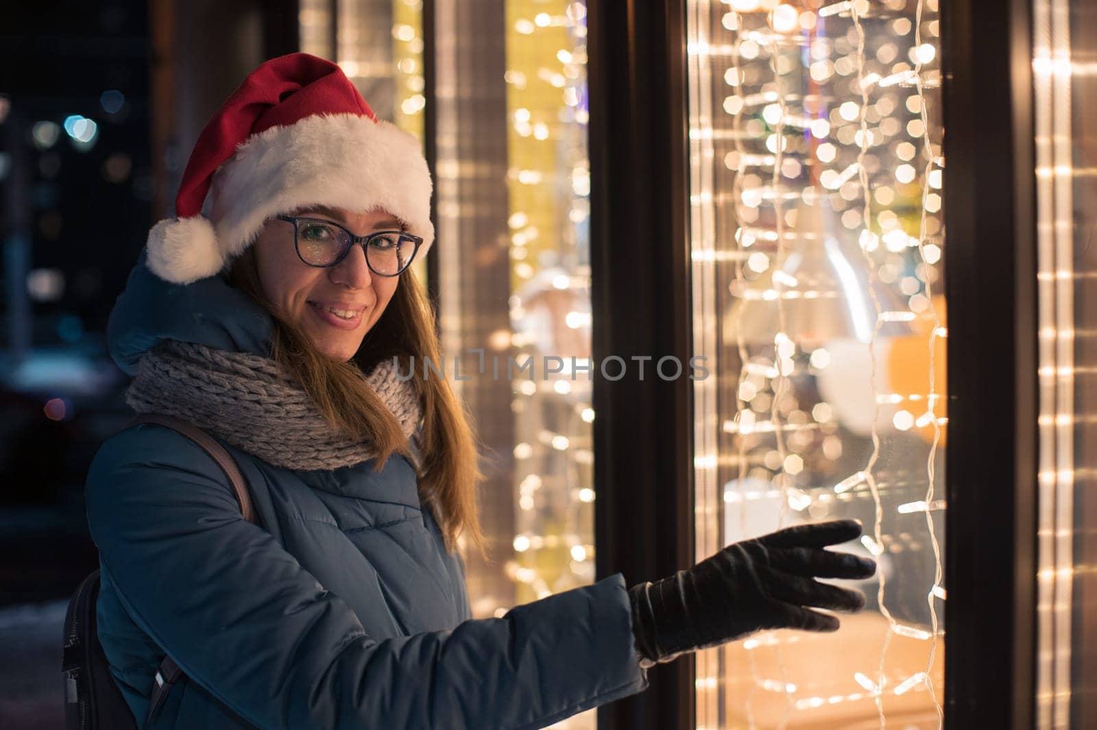 Woman in Santas hat looking and dreaming in illuminated shop window. Xmas presents holidays, or shopping on New Year or Christmas concept