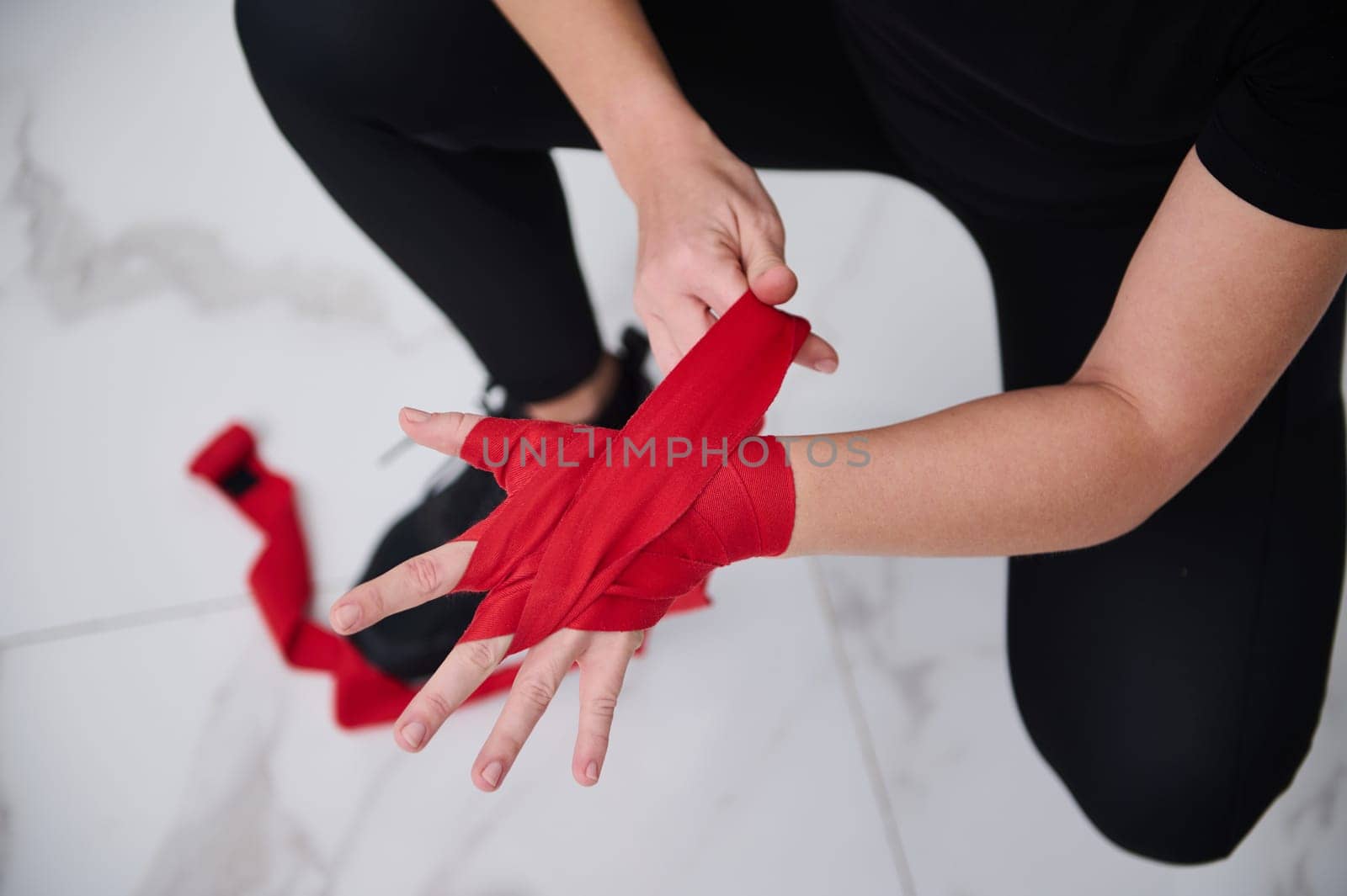 Close-up female boxer fighter tying tape around her hand preparing to box. People, challenge, competition, martial art and sport concept. View from above