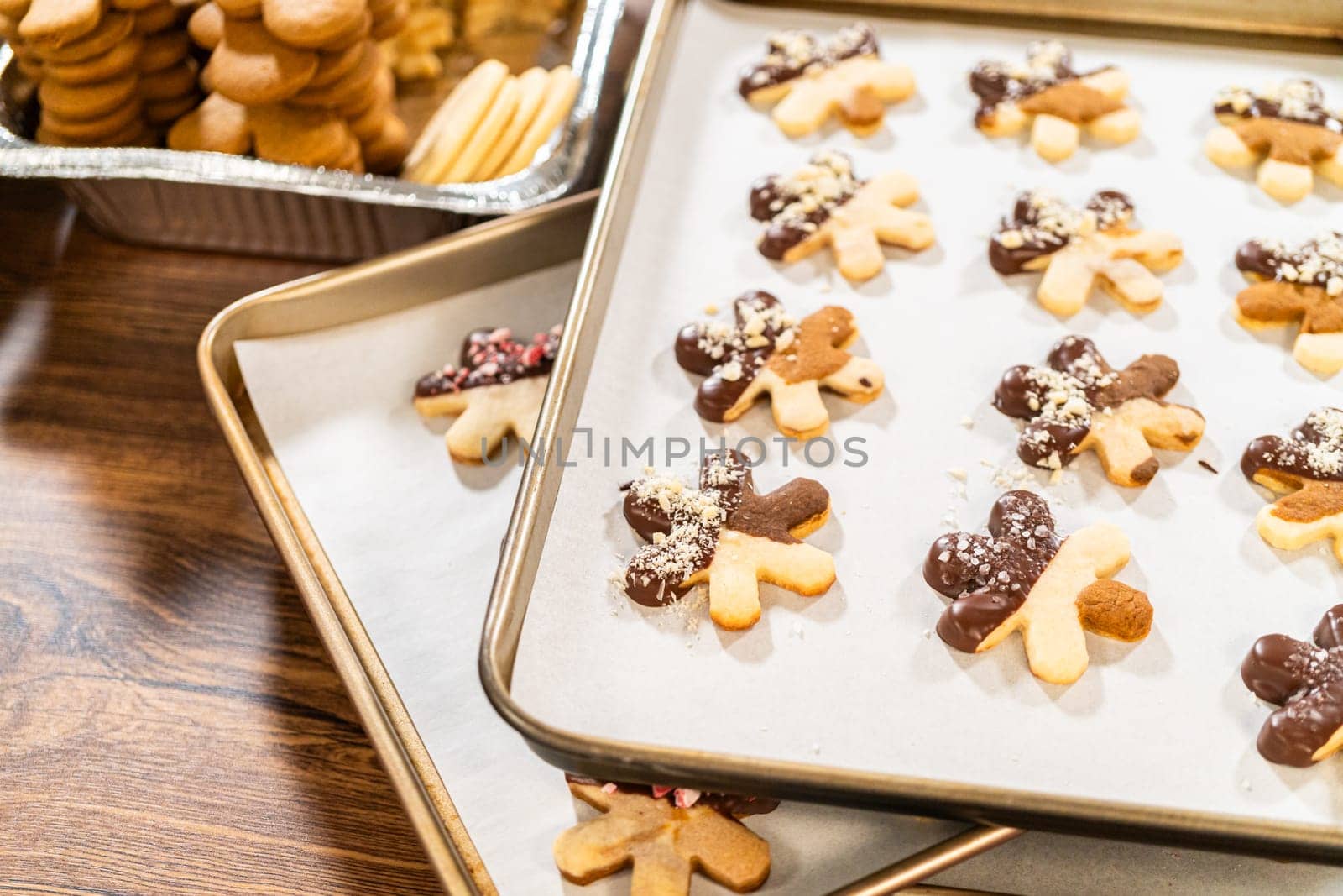 Creating cutout sugar cookies, partially dipped in chocolate and topped with hazelnut pieces, placed on parchment paper.