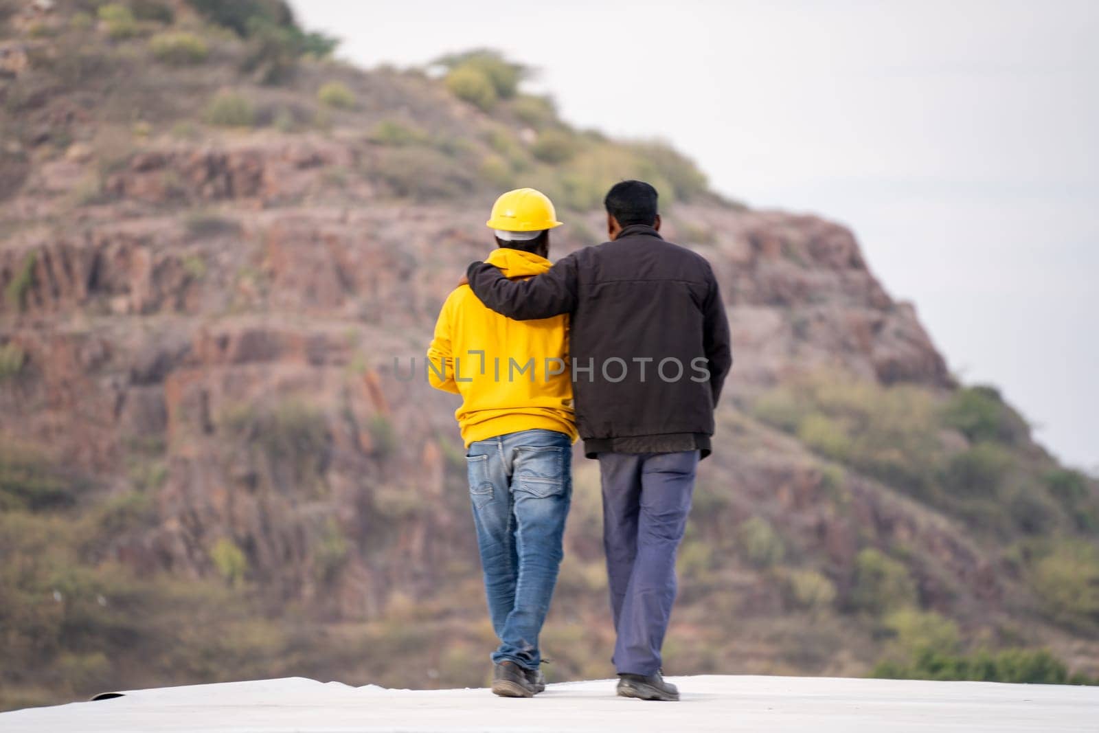 Man friends talking to person with construction hat helmet and visibility clothing showing mountain to build through by Shalinimathur