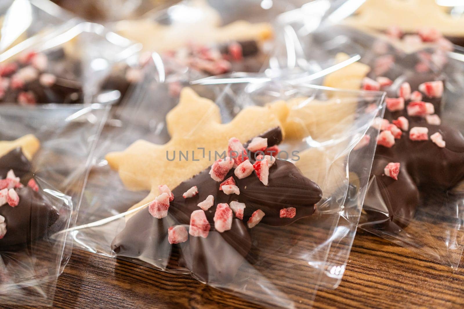 Carefully packaging Christmas cutout cookies, half-dipped in chocolate and presented in clear cellophane wrapping, perfect for festive gifting.