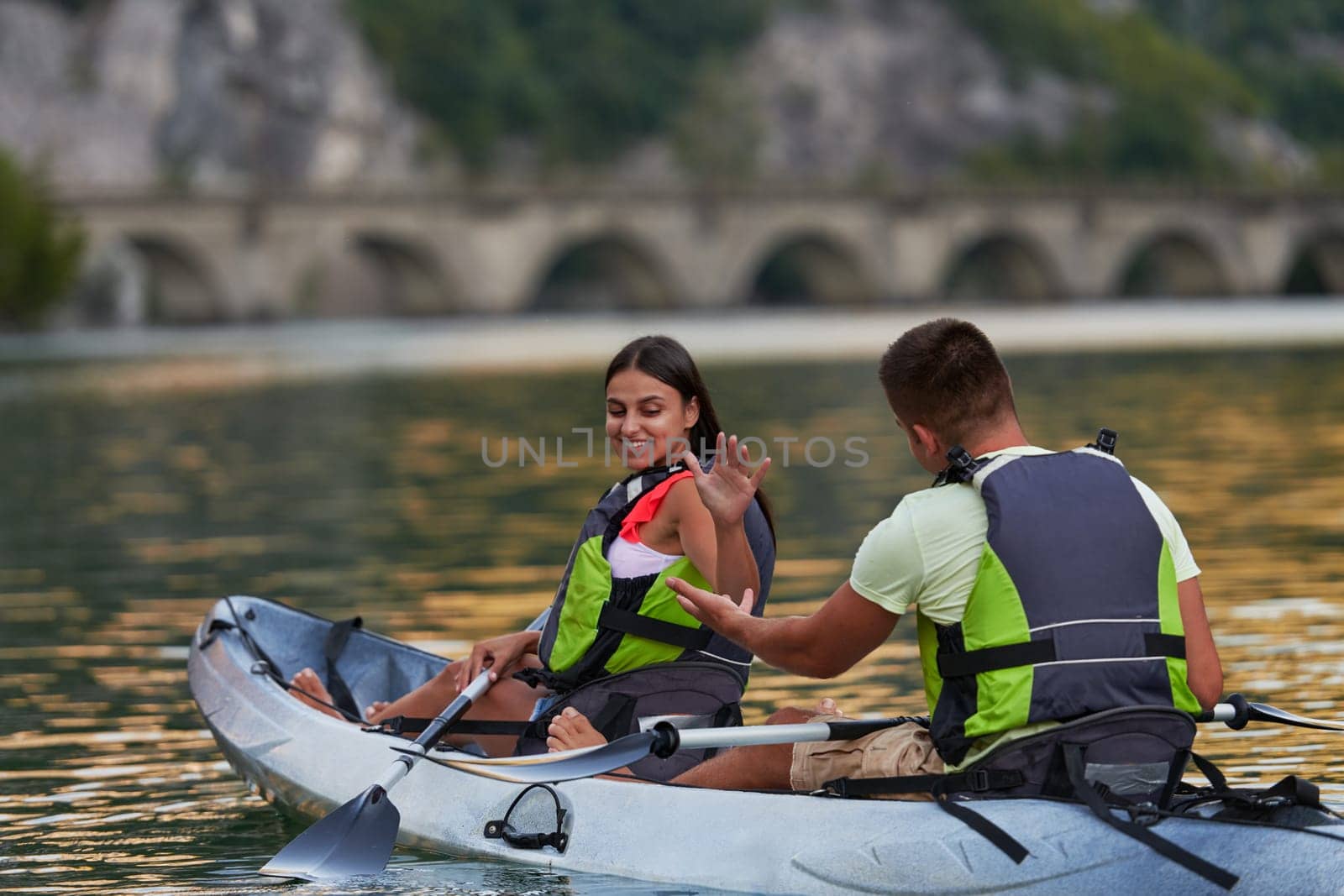 A young couple enjoying an idyllic kayak ride in the middle of a beautiful river surrounded by forest greenery.