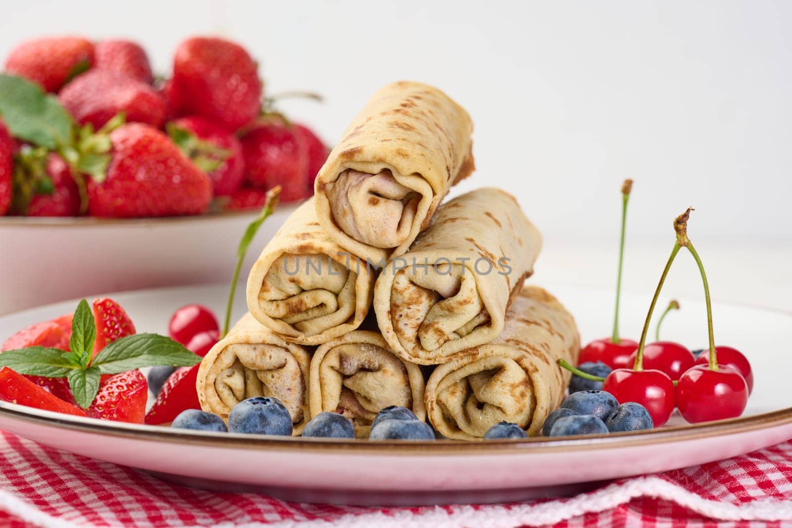 Stack of fried crepes with filling on a round plate, white table