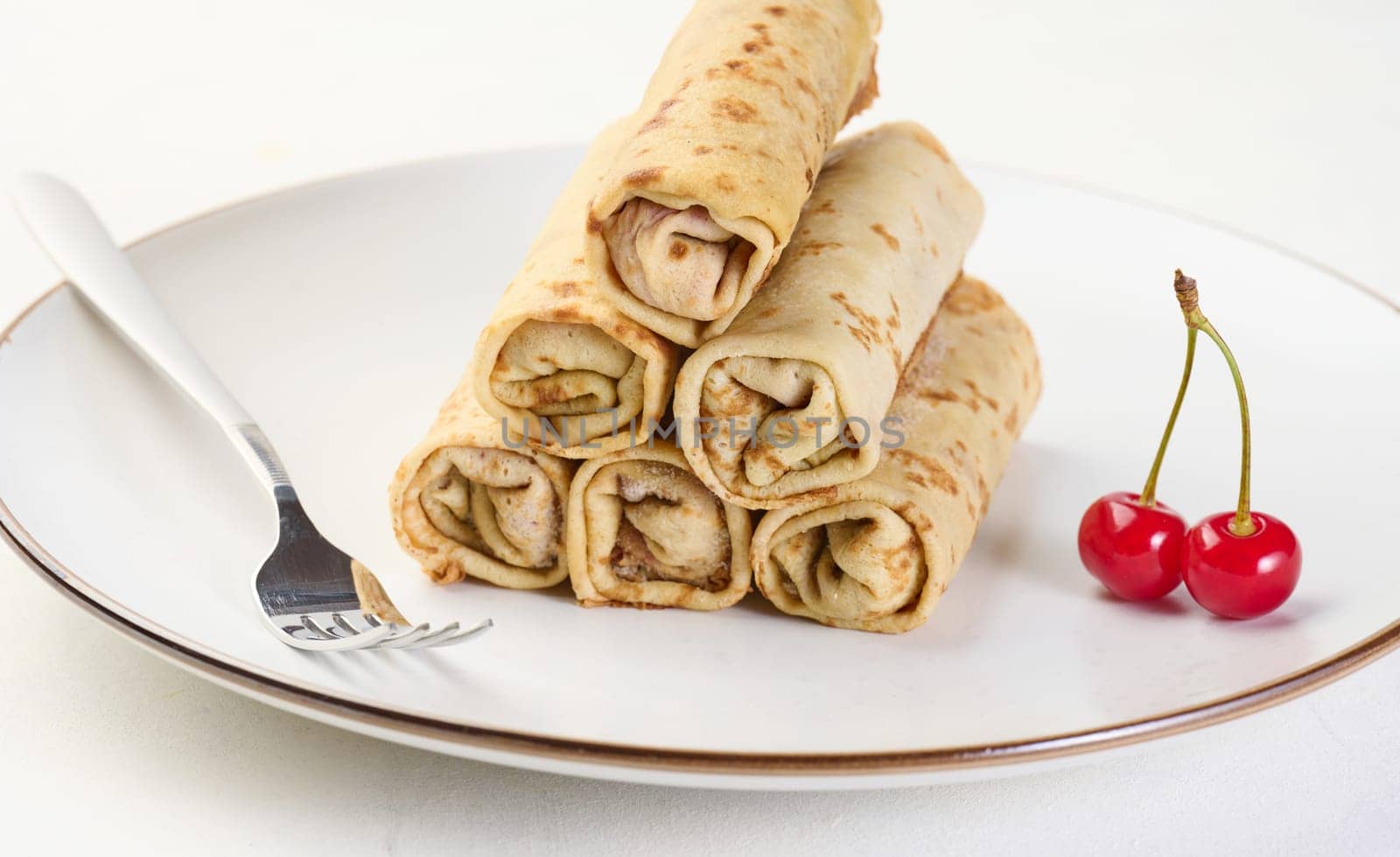 Stack of fried crepes with filling on a round plate, white table