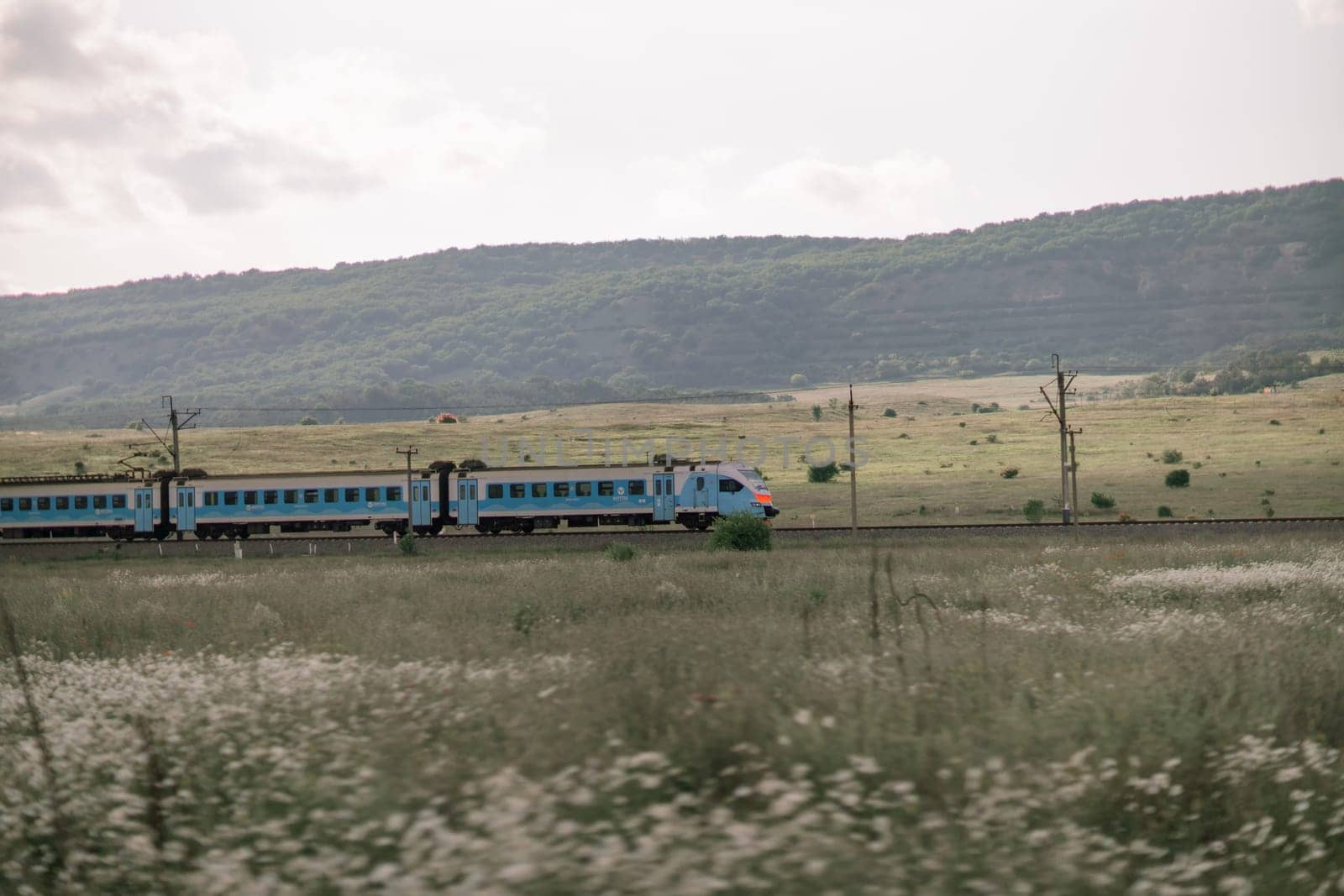 A train is traveling through a field of grass. The train is blue and has a red stripe