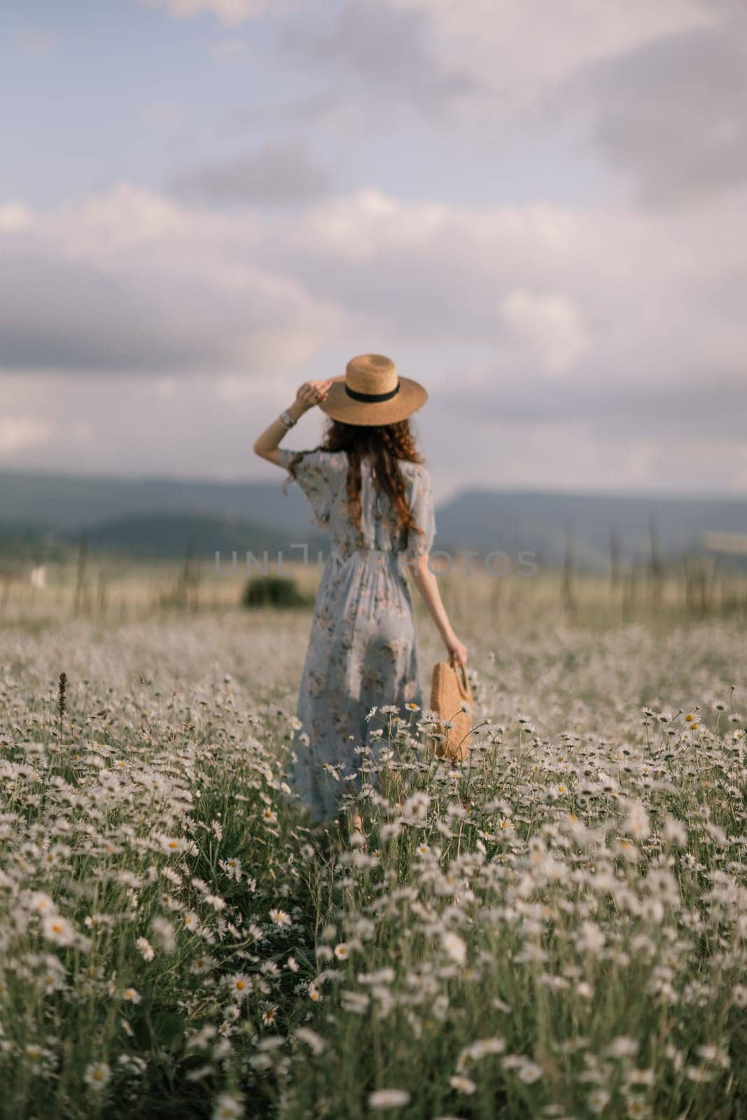 A woman is walking through a field of flowers, wearing a straw hat and carrying a basket. The scene is peaceful and serene, with the woman standing in the middle of the field by Matiunina