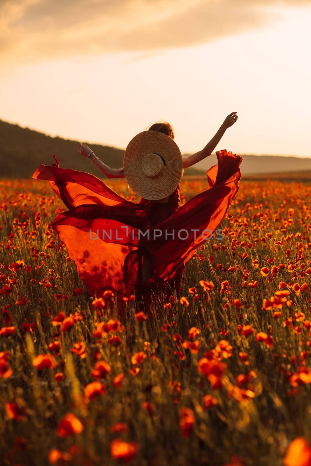 A woman in a red dress is running through a field of red flowers. She is wearing a straw hat and has her arms outstretched. The scene is bright and cheerful, with the sun shining down on the flowers