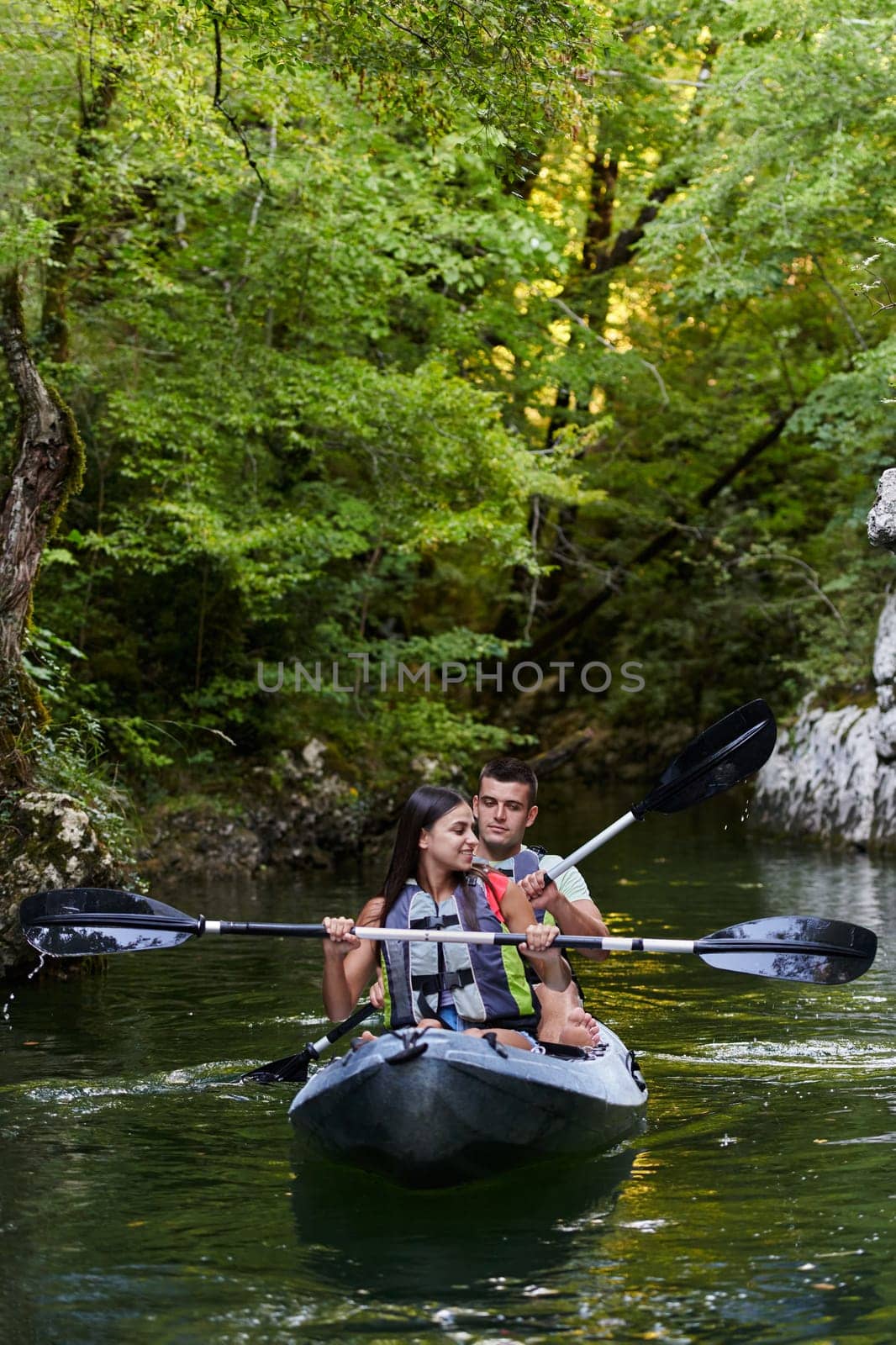 A young couple enjoying an idyllic kayak ride in the middle of a beautiful river surrounded by forest greenery.